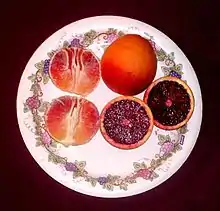 A plate showing three blood oranges: one whole, one peeled, and one sliced in half