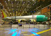 Airplane assembly hall, featuring an unpainted metallic twin-jet aircraft, a presentation podium, and arranged audience chairs