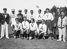 Photo of twelve men, seven standing and five crouching, inside a stadium