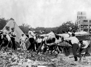  Police with batons confront demonstrators armed with bricks and clubs. A policeman and a demonstrator wrestle over a US flag.