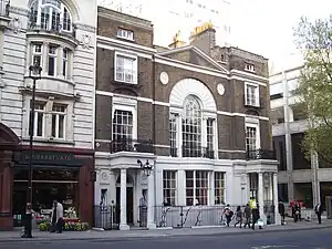 the facade of a three-story Georgian building in London. The building is in brown-red brick, with cream-coloured Portland stone edging, portico and columns