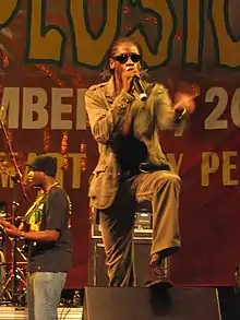 Man with cornrows singing into microphone onstage