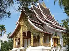 Stone building with golden decorated entrance, stacked and very steep roofs.