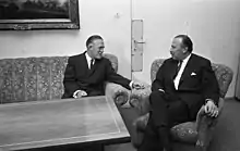 Two middle-aged men sitting in a sofa and a chair around the corner of an empty table