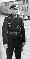 A young man wearing a peaked cap and black military uniform with an Iron Cross displayed at the front of his uniform collar.