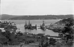 A large warship is tied to the dock in a narrow channel of water.