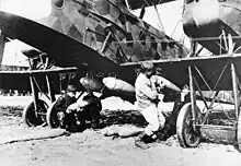 Two men in work clothing attach bombs to the underside of an aeroplane