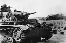 German tank in the foreground with a burning wreck in the back