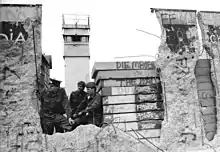 East German border guards look through a hole in the Berlin Wall in 1990