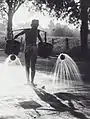 A worker waters a road in the Dutch East Indies