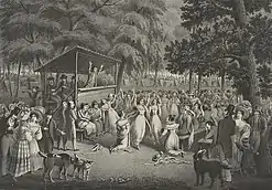 A black-and-white image depicting a Methodist camp meeting during the Second Great Awakening. A preacher, his arms raised up, sermonizes on a small wooden stage with a canopy over him. The audience is a huge crowd of people, mostly standing, though a few sit on benches. Some seem to talk to each other, some seem to listen raptly. One man kneels, as if praying. One woman has swooned and fallen over and is held up a man. There is a mix of dress, with some people in very fine clothing. The setting is apparently a forest, as large trees frame the image. In the background, dozens of tents are visible.