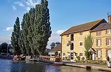 Old mill building by a canal with several anrrow boats moored alongside