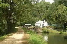  Photograph of a dirt towpath beside a canal with a lock with a house in the background