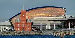 Image of Cardiff Bay's Waterfront from the bay, with the 1897 Pierhead Building to the left, the Senedd building to the right, and the coppery roof of the Millennium Centre behind them.