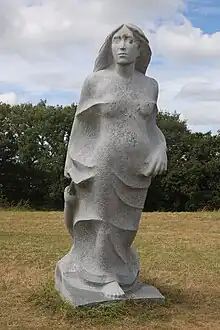 A statue of Clervie leaning forward with a goose neck wrapping around her calves and a goose head looking up at her. She is depicted in a long, single piece, linen or silk robe