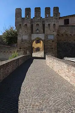 A pointed arch castle entrance with crenellations at the top. The brick is grey-red.