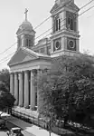 Black-and-white photograph of a large church with a portico; two twin bell towers extend from both sides of the building.