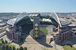 A large open-air stadium with a split roof supported by a pair of white arches and a tall central tower