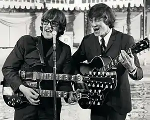 Chad and Jeremy standing at a microphone, singing and playing guitars