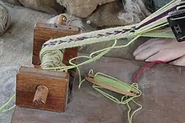 Belt or band shuttle, a short shuttle used for inkle weaving. This extra-sturdy shuttle is also used at a batten, to beat the newly woven weft against the previously woven fell.