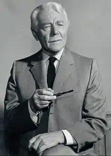 A black-and-white photograph of a man in a suit and tie with white hair and a pipe