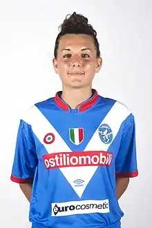 Woman with black hair in blue and white football kit.