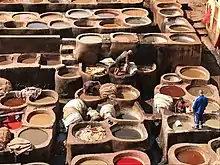 Large open-air vats of color dyes with tannery workers amongst them