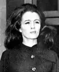 A black and white close-up photograph of Christine Keeler, a slim woman wearing a dark coat with long dark hair and a slight smile, looking to the left.