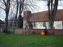 A flint and rendered church with a red tiled roof and a tower with a brick upper part