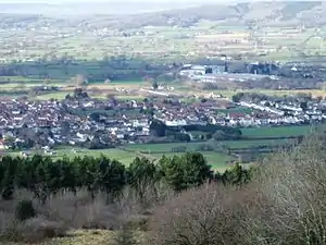 Multiple houses in Lower Langford, mostly with red roofs seen in a valley between the vegetation in the foreground and the hills beyond