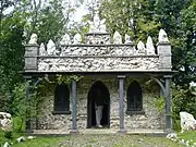 a vary ornate single-story building clad with shells with the front overhang supported by grey pillars