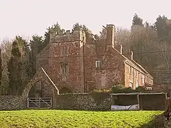 Red brick building with tall chimneys. In the foreground is an arched gateway.