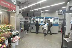 View of the fare control area at ground level. There is a station agent booth in the background and a florist to the left.