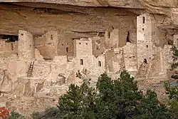 Ruins of stone buildings under a cliff