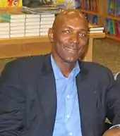 A man, wearing white shirt with a logo and the word "NBA PLAYERS" on the front, is standing and posing for a photo.