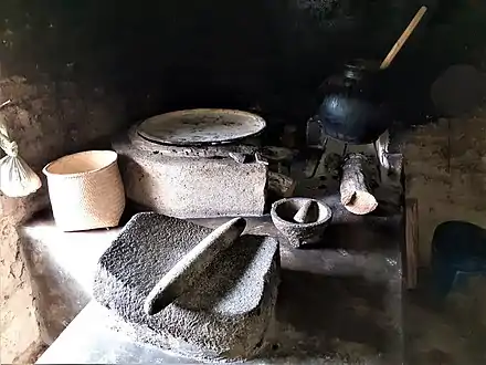 Contemporary indigenous kitchen with metate in the foreground, comal, palm tenate, molcajete (stone mortar) and a clay pot. San Juan Achiutla, Oaxaca, México, 2020.