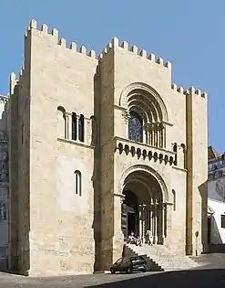 The Old Cathedral of Coimbra, Portugal, is fortress-like and battlemented. The two central openings are deeply recessed.