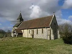 A mainly flint church with red tied roofs and bellcote with a spirelet