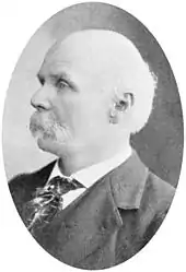 A black and white side profile portrait of an elderly man with a mustache, and wearing a suit and tie