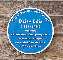 Blue plaque reading "City of Durham Parish Council. Daisy Edis (1888–1964). Pioneering Durham professional photographer lived at 142 Gilesgate and worked from her studio at 52 Saddler Street"