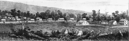 In the foreground, fields and three figures. In the background, rows of agricultural workers' huts