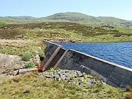 A concrete dam head, with spillway, surrounded by hills