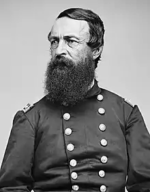 Black and white photo of a full-bearded, glaring man wearing a dark military uniform with two rows of buttons.