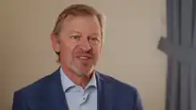 bearded man in blue shirt and jacket talking to camera