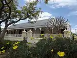 Church Street and Van der Stel Street are two parallel thoroughfares in Tulbagh. In these old streets a number of buildings have survived that give a true reflection of the character of the village in the eighteenth century. One of them is now the public library. Like De Wet House, it stands on a portion of a plot in Church Street that was sold by the Church Council in 1796 to defray the cost of the new, larger church. The plot was trans ferred to Jacob de Bruijn, who sold the northern portion of it to Christiaan Willem Broodryk in 1805. It was Broodryk who built the T-shaped house with a concavo convex front gable. The "brandsolder" with reed ceiling in the front room is especially worthy of mention. Type of site: House Previous use: Residential. Current use: House. Because of its architectural merits and situation, this historic house forms an important element in the street scene of the restored part of Tulbagh.