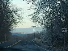 Ground-level view of a highway lined with ice-covered trees. A sign on the right-hand side bears the route's designation.