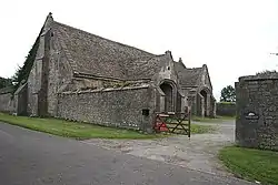 Gray stone building with two arched porch entrance doors. Separated from road by stone wall.