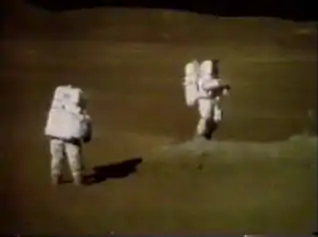 TV camera still of Duke (left) and Young on the rim of Plum.  Duke remarked at this time, "John, you are just beautiful. That is the most beautiful sight." Young is standing next to a boulder from which sample 61295 was taken.