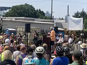 Earl Blumenauer speaks at the opening ceremony for his namesake bridge, as Jo Ann Hardesty and others sit on the stage near him