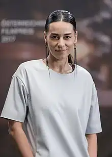 White female with dark, tied-back hair, wearing a white t-shirt and long earrings, smiling directly at camera